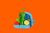 An open lunchbox filled with vibrant green bell peppers, lettuce, tomato, and a slice of lemon set against a contrasting orange backdrop.