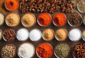 Top view of various assorted mix of coloured powdered spices in bowls placed on wooden table displayed in market
