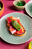 From above of traditional Spanish tapas of jamon and padron pepper on slice of toast on plate