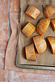 Top view of slices of tasty homemade pumpkin placed on a metal baking tray drizzled with olive oil on a table in a bright kitchen