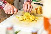 High angle of hands of an anonymous chef slicing yellow potatoes on a white cutting board in kitchen