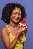 Friendly charismatic African American female model smiling with closed eyes while holding slice of sweet watermelon