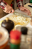 High angle of hands of an unrecognizable chef meticulously chopping onions on a white cutting board and an array of spices in the foreground