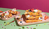 From above tasty sweet waffles topped with berries fruits sauce and cream served on pink tray on colorful table background in light kitchen