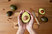 Top view of crop anonymous person holding avocado over wooden table indoor