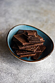 High angle of pile of pieces of different kinds of chocolate placed in crop ceramic bowl on gray blurred table