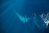 Großes Netz mit Seilen schwimmt im tiefblauen Meerwasser unter Sonnenlicht beim traditionellen Fischfang in Soller