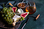 Top view assorted yummy snacks with cheese and served on plate placed on above wooden board with grapes and figs and jam