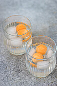 From above of pair of transparent glasses filled with melon spheres in iced beverage and placed on gray surface in daylight