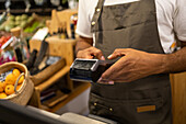 Unrecognizable male salesman wearing an apron standing by the counter while working in a shop in blurred background