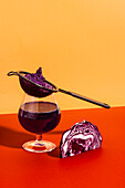 Gesundes veganes antioxidatives Getränk aus extrahiertem Rotkohlsaft in einem Glas mit Sieb auf rotem und gelbem Hintergrund