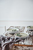 Ceramic bowls of green cream soup with sage served with seeds and herbs on wooden table with shabby surface against white background