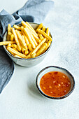 High angle of ceramic bowls with French fries and sour sweet sauce placed on white surface near napkin