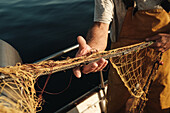Unkenntlich gemachter männlicher Fischer in Uniform, der auf einem Schoner in Soller in der Nähe der Baleareninsel Mallorca mit einem Netz auf Fischfang geht