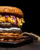 Closeup of crop hamburger with macaroni and cheese placed on wooden tray on table against dark background