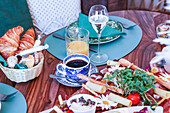Ein gut ausgestatteter Brunch-Tisch mit einer Vielzahl von Speisen, darunter frische Croissants, Aufschnitt und Käse, begleitet von Kaffee, Saft und Wein