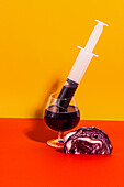 Antioxidant healthy juice of red cabbage vegetable extracted in glass with syringe on bright backdrop with cabbage