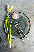 Top view of table setting with fresh tulip flowers on concrete background