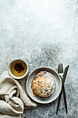 Top view of sweet almond pastry between fork and knife and napkin with cup of green tea against gray background