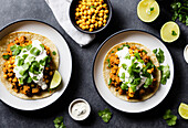 Top view of tasty tortilla flatbread with chickpea and meat topped with cilantro and sour cream served on plates with cutlery over grey table background. Generative AI