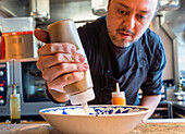 Crop focused man in black clothes and apron using batter dispenser to add ingredients inside dishware on wooden table in restaurant at Zermatt Switzerland