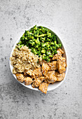 Top view of appetizing crispy fried chicken and veggies served on white bowl over grey background with copy space