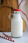Raw cow milk in vintage closed bottle near drinking straws on gray surface against blurred background