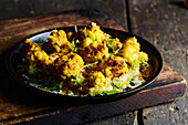 High angle of appetizing roasted cauliflower with green herbs served on black plate placed on wooden board