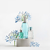 Beauty products in blue glass spray and pipette bottles standing on podium with flowers and petals at white background. Cosmetic setting with serum,perfume fragrance and toner. Front view