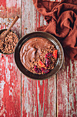Top view of bowl filled with chocolate smoothie placed near red fabric on wooden table