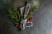 Top view of Christmas composition of fork and knife wrapped in handkerchief near green fir sprigs placed on gray background