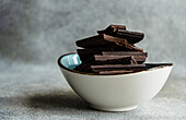 Pile of pieces of different kinds of chocolate placed in ceramic bowl on gray blurred table