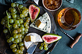 Top view assorted yummy snacks with cheese and served on plate placed on above wooden board with grapes and figs and jam