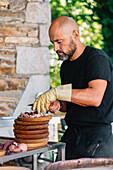 Side view of A bearded chef in gloves meticulously slices boiled octopus on a wooden plate while celebrating a local festivity in Galicia