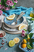 Von oben dekorierter Tisch mit verschiedenem Geschirr und Besteck mit frischen Zitronenscheiben auf blauem Betonhintergrund neben Serviette und Besteck mit Blumenstrauß