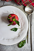 Top view of whole fresh red apple with leaves on plate near cutlery on gray table