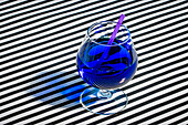 Hoher Winkel eines blauen Cocktailglases, garniert mit einem Strohhalm, serviert auf einer gestreiften Stoffoberfläche