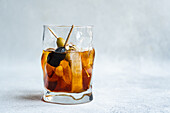 Transparent glass cup with whiskey alcoholic drink and stick of olives cocktail with ice cubes