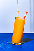 Close up shot of glass of fresh orange juice cocktail with spill on blue background