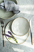 Top view of autumnal table setting with ceramic bowl and plate with lavender flowers between fork and knife against gray surface