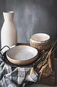 Ceramic bowls and vase near napkin on wooden board placed on marble table against gray background at rustic kitchen