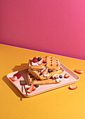 From above tasty sweet waffles topped with berries fruits sauce and cream served on pink tray on colorful table background in light kitchen
