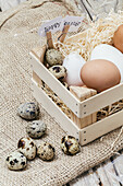 A wooden basket filled with various eggs and a sign reading 'Happy Easter' on rustic burlap.