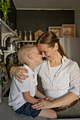 Loving Caucasian mid adult mother looking at her son lovingly cute adorable son while together in kitchen during weekend