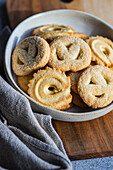 From above fresh homemade baked butter cookies placed in a bowl on a wooden cutting board beside a gray napkin, set against a minimalist concrete background