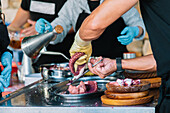 Closeup of anonymous street food vendors in Galicia expertly cooking traditional octopus, showing the chefs cutting and garnishing the sliced tentacles with sauce
