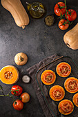 Top view of ripe whole and sliced butternut squash and sliced tomatoes placed together on plain surface and on glass tray in kitchen at home
