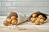 Sweet panellets in newsprint cones placed on wooden table against white tile wall