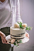 Unrecognizable female demonstrating appetizing cake decorated with flowers and sprigs on wedding day