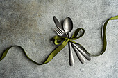 Top view of vintage cutlery set placed on gray surface with green ribbon in light kitchen